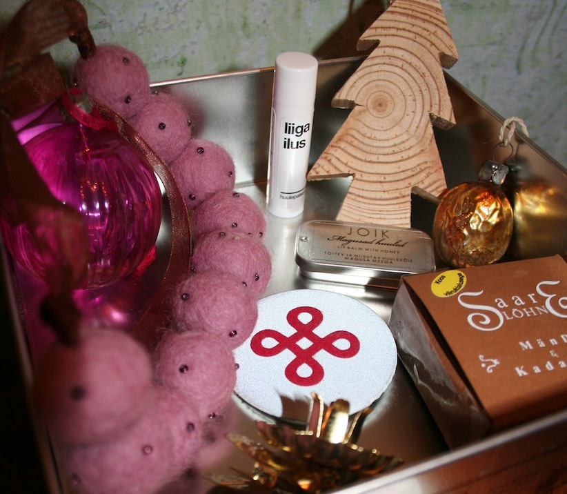 Päri/päeva ("daywards"), i.e. clockwise from the top are: MO$HI's "liiga ilus" lip balm (huule/palsam), a wooden tree ornament, a tin with JOIK huule/läige (lip gloss), a Soviet-era glass ornament in the shape of a walnut (kreeka/pähkel), incense (viiruk), a reflector pin (helkur), a candle holder for the tree (Danger! Danger!) and necklace made of felted wool, hugging another antique glass ornament. Photo: Riina Kindlam