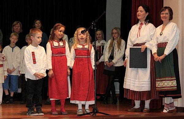 20. jaanuaril Luksemburgi Eesti Kooli avaaktusel loevad Olivia Saare luuletust "Mis värvi on kodu" vasakult Tim Vunder, Nora Kpalobi ja Melinda Koch. Kõrval on kooli juhataja Mari-Liis Kivioja ja eesti laste laulustuudio juhendaja Anneli Aken. Foto: Meelik Mallene, Luksemburgi Eesti Seltsi president