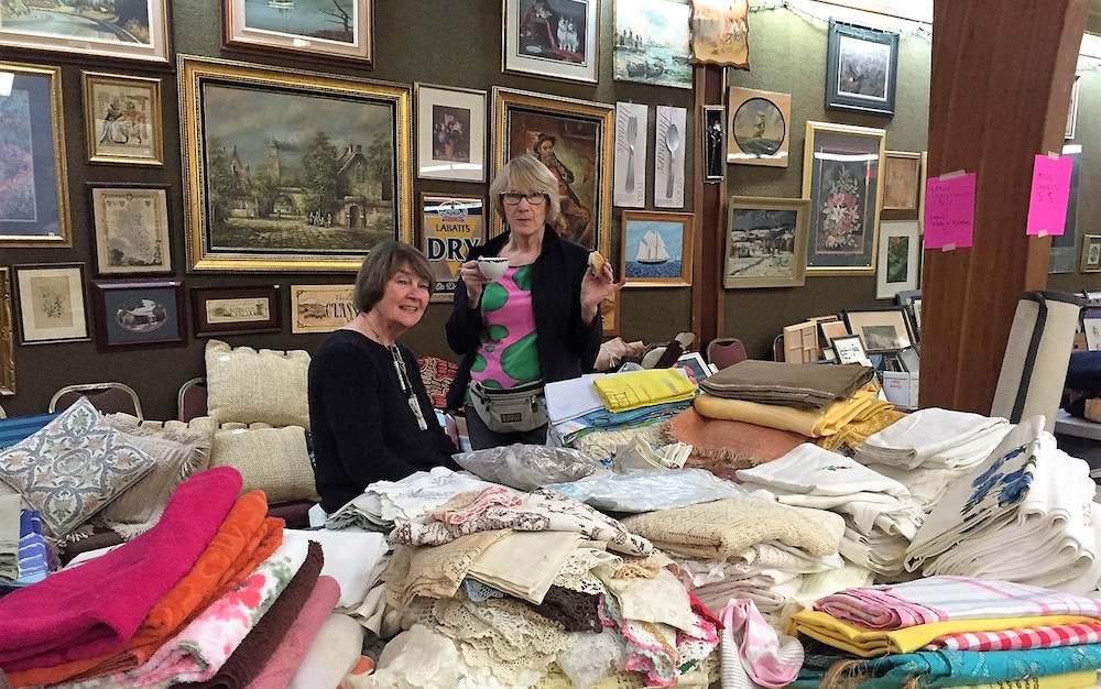 What’s this? An art gallery? Yes! A bedding store? Yes!  Art and fabric enthusiasts Anu Turnbull and Maaja Matsoo took on the „giant” task of setting up and pricing items in the well-stocked art and bedding departments at AKEN’s Giant Rummage Sale. Photo: Kristiina Valter