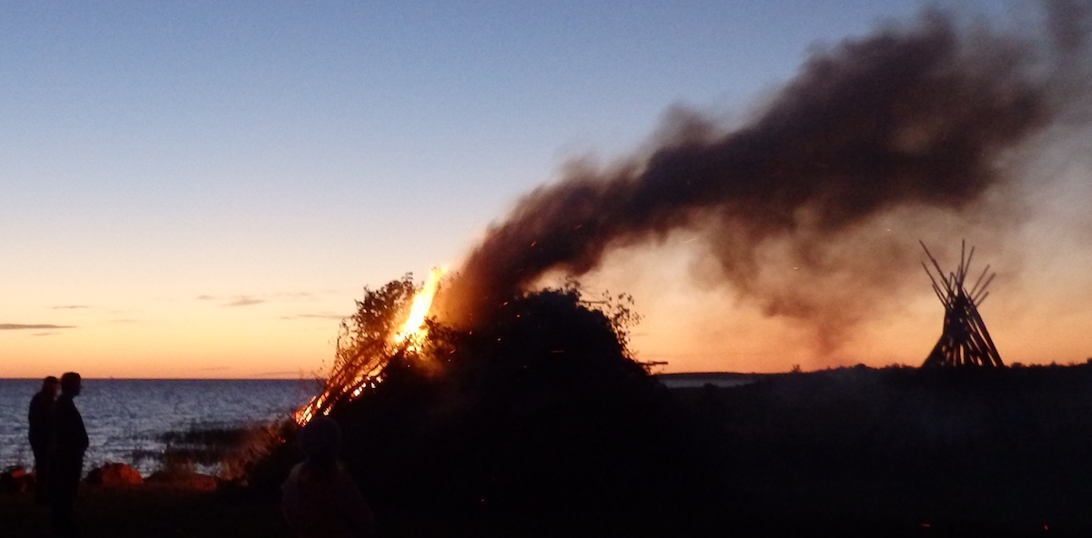 Vaatamata valjule tuulele süüdati Koguva sadamas Muhu saarel tänavusel muinastulede ööl 27. augustil võimas lõke. Õnneks oli vett lähedalt võtta ja tulel hoiti silm pikalt peal. Taevas mere kohal veel kumas ja vasakul pool vaatevälja, Saaremaa idarannikul, hakkasid pea paistma sealpoolsed lõkketuled. Foto paremas ääres, suitsu seest paistavad püstilaotud mõrravaiad, mida kogenematu linnainimene esialgu ekslikult püstkodadeks pidas - foto: Riina Kindlam (2016)