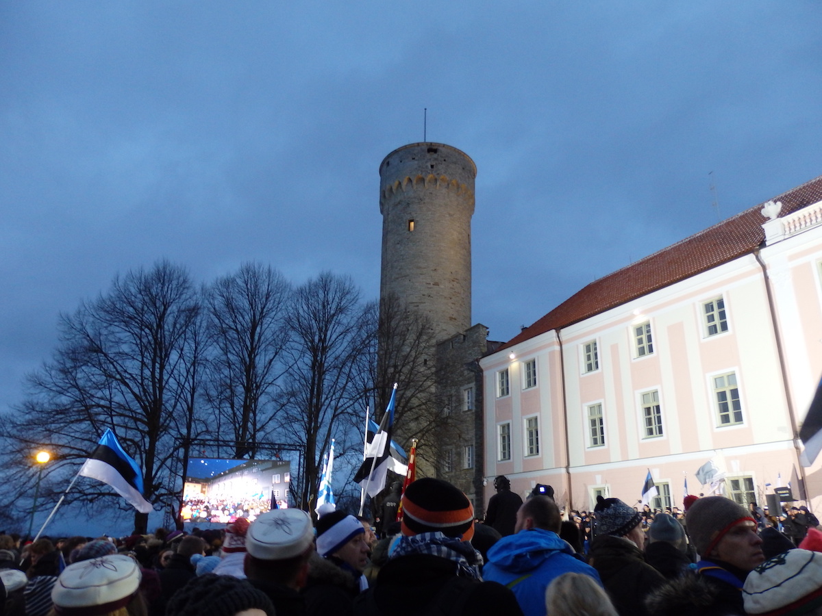 Hetk enne päikesetõusu ja lipuheiskamist Pika Hermanni torni kell 07.35. Tänavu koguneti Toompea lossi hoovi asemel suuremale alale lossi kõrvale Kuberneri aeda. Taamal on näha suurt tele-ekraani kõnelejate paremaks nägemiseks, ees kõrgkoolide ja üliõpilasorganisatsioonide värvimütse ja korporatsioonide tekleid ning lippe. Väikesest torniaknast paistab sooja valgust. Foto: Riina Kindlam (2017)