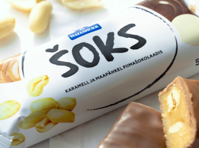 Eesti oma Snickers. Šokolaadi hellitus- ehk hüüd/nimi kõne/keeles on ŠOKS. Eesti oma maiuse/tootja kommi/vabrik Maias/mokk (*,,sweet lip“* tähenduses *sweet tooth*) valmistab alates 2001. aastast mitmeid just selle/nimelisi maiustusi, kaasa/arvatud juuresolevat šokolaadi/batooni, mis on oma sisult ja vormilt väga sarnane üle/maa/ilmselt müüdud USA tootele. Mars'i perekonna kommivabrik sai alguse Tacomas, Washingtonis aastal 1911 ja Snickers sai oma nime perekonna lemmikhobuse järgi ning toodi turule aastal 1930. Foto: Maiasmoka Facebooki lehe/külg (N.B.! See Maias/mokk ei ole seotud aja/loolise Maiasmoka kohvikuga Tallinna vana/linnas. Seal, kus asub kohvik ja martsipani/tuba hakkas Kalevi ja Kawe eel/käija valmistama maiuseid aastal 1806. 2010 sai AS (aktsia/selts) Kalev Norra päritolu rahvusvahelise Orkla kontserni liikmeks ehk osteti ära, kuid maiustuste tootmine jätkub Kalevi kauba/märgi all.) 