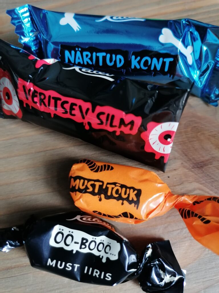 Midagi pole öelda, vaimukus (wit, humour) on laes ehk kõrgel tasemel. Halloweenikommi/segu pakis on NÄRITUD KONT, mis iga/päevaselt on šokolaadi ,,batoonike“ (pikliku kujuga komm) nimega Kaseke; VERITSEV SILM, igapäevaselt marja/maitseline marmelaadi/komm Mari; MUST TÕUK, tavaliselt Drako koola/maitseline (cola flavoured) närimis/komm ja ÖÖ-BÖÖÖ must iiris (caramel), tava/nimega Kiss- Kiss, mis aga tavaliselt ei ole musta värvi. Kommid on ka endale justkui kostüümid selga tõmmanud. Paki sees ei ole konti, silma/muna ega tõuku. Tõuk on antud juhul (in this case) ussikese moodi putuka vastne (larva). See komm ei ole aga must, vaid valge muna, mille seest siis tõotab (promises) ilmuda must tõuk. Pehme, veniv ja koorene (creamy) iirise/komm on see-eest must nagu öö. Tekib lootus (või kahtlus), et tegemist on lagritsaga (licorice), aga ei. Soomes ja teistes Põhja/ maades, kus must (ka soolane) lagrits on au sees, oleks see kahtlema- ta lagritsa/komm, Eestis aga kahjuks (või õnneks) mitte. (Foto: Riina Kindlam)