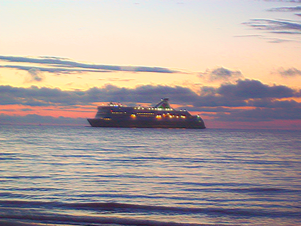 A ferry approaches Tallinn across calm waters at sunset, with warm lights glowing against a dramatic, cloud-filled sky. (source: Keeleklikk)