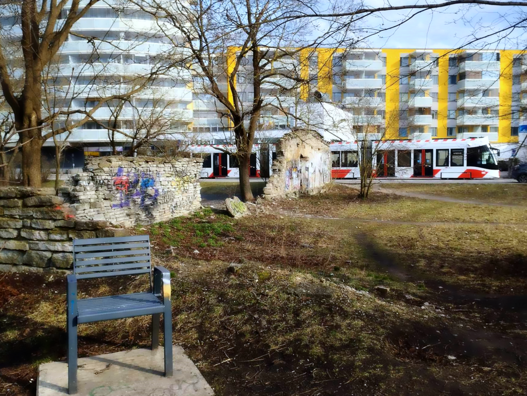 A view toward Tondi Street, where a tram glides past crumbling walls and a lone metal bench, the spring earth still waking from winter. Photo: Jerry Mercury