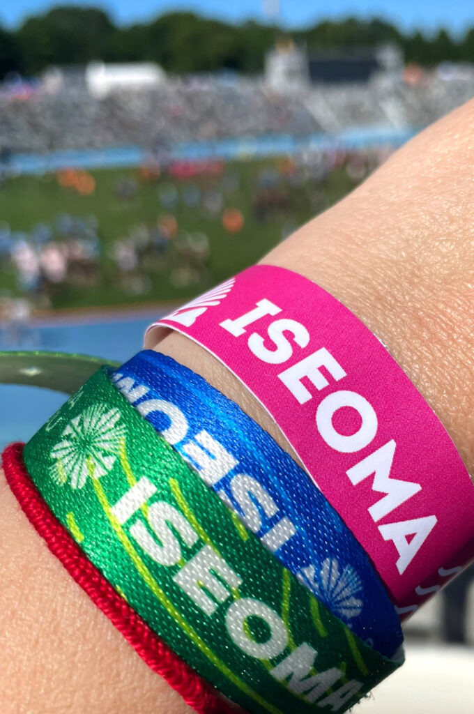 Selle suve laulu- ja tantsu/peo osa/võtjate (participants) käe/paelad nägid välja sellised. Alt (from the bottom): roheline on tantsija (dancer’s) pael, sinine laulja (singer’s) pael ja roosa näitab, et kandja oli vaba/tahtlik (volunteer) TOITLUStus/alal (in the participants’ eating area). Taustal (in the background) paistab häguselt (blurrily) Kalevi staadion, kus toimuvad tantsupeod. Foto ja käe/vars (arm): Kersti Vahter