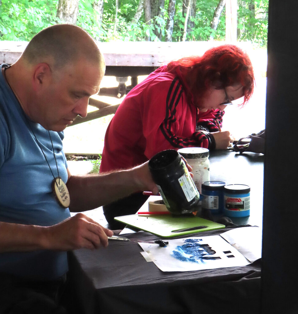 Võimalusi maalida, joonistada ja trükkida, k.a. kleepsusid (stickers) tõi kaasa Jõekääru suvekodus aastaid laste loomingulisust julgustanud Andres Musta (vasakul). Töö käis Eestist kaasa toodud värske muusika saatel. Kõrval lõikab Tuule Kindlam Sillak Tallinnast pehmet linoollõike kummiplaati. Foto: Riina Kindlam