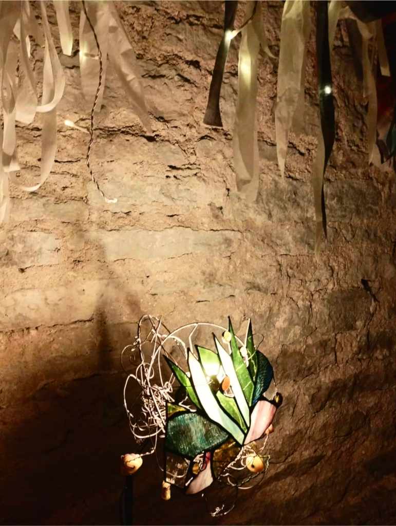 Maire Valdma’s stained-glass lamp with green leaf-like forms, beneath fabric ribbons (photo: Jerry Mercury)